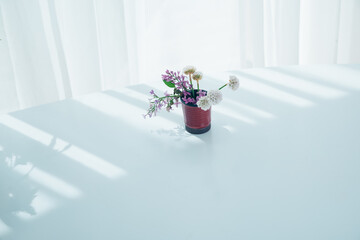 Little brown cup with different flowers on white surface in lines of light and shadow. Spring flowers in the cup.