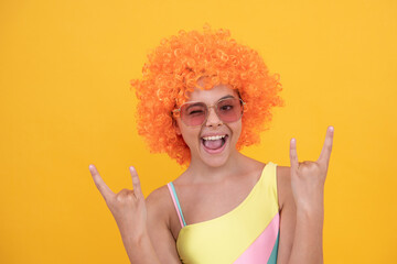 happy cool teen girl in sunglasses wearing orange curly wig hair on yellow background, childhood.