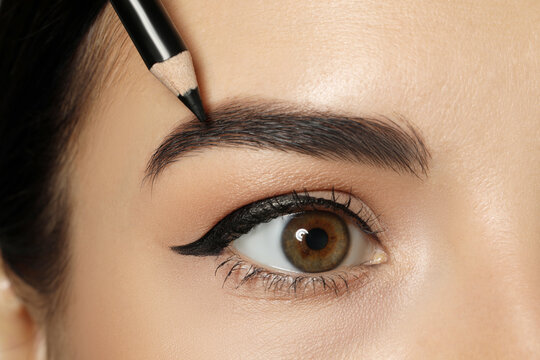 Young woman correcting eyebrow shape with pencil, closeup view