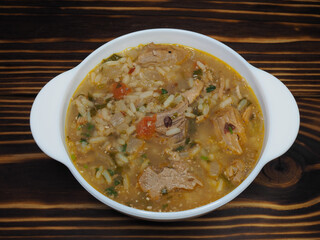 Hot kharcho soup with meat, rice and vegetables, spicy herbs in a white bowl on a wooden table, flat layout. A traditional classic dish for lunch. Rich thick broth with beef, Georgian cuisine