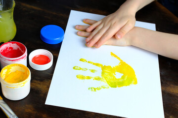 close-up hand of a small child leaves colored palm prints on white paper, creative creativity concept, fine motor skills, patience and perseverance