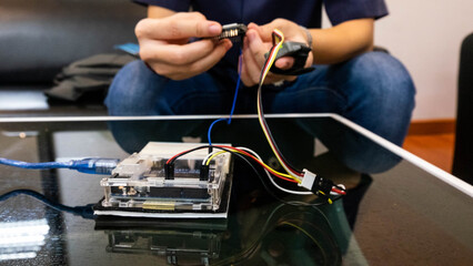 Close-up of a student’s hand connecting wires on a breadboard with an Arduino board while...