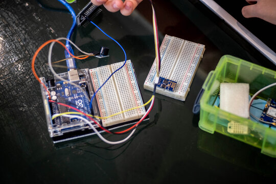 Close-up of a person assembling an Arduino Uno circuit using a breadboard and jumper wires. One hand carefully holds a module, while the other hand balances the components during setup.