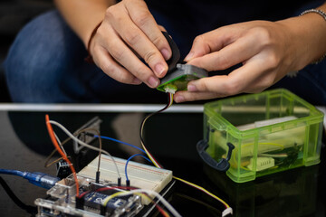 A detailed close-up of hands building an Arduino Uno electronics project. Wires, sensors, and...