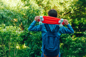 close up stylish man carrying the penny board on the background of green trees