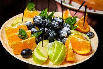 Sliced apples, oranges and black grapes with mint leaves on a plate. Close-up, selective focus
