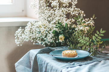 Lemon tart on a blue plate on a striped cloth, decorated with  white flowers bouquet scene