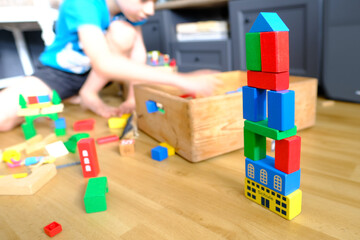 small child, boy builds towers and buildings from colored wooden figures, concept of housing construction, mortgage, insurance, happy childhood, children's games