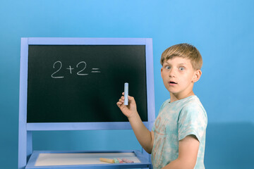 The boy solves the math equation 2 + 2 written on the blackboard. The child does not know the...