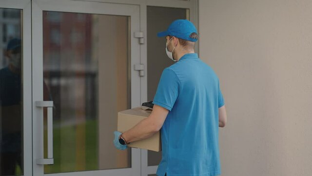 Pandemic and online order delivery A delivery man wearing a protective mask and gloves passes the parcel to the customer and receives a contactless payment via tas