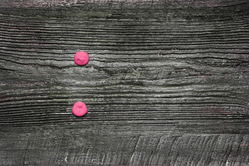 Two pink dots, painted with squeezed paint from a tube on an old wooden board, a colon punctuation...