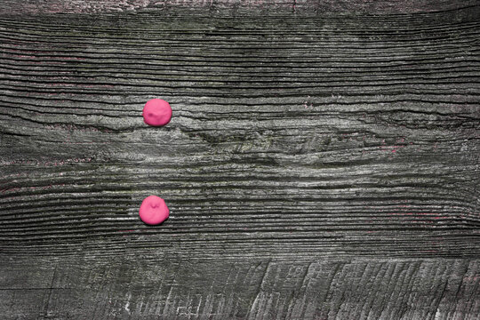 Two pink dots, painted with squeezed paint from a tube on an old wooden board, a colon punctuation mark or mathematical division sign.