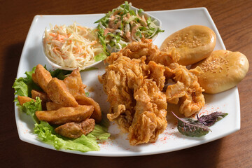 Crispy fried chicken pieces in breadcrumbs on a plate with potatoes, bread and salad, on a wooden table