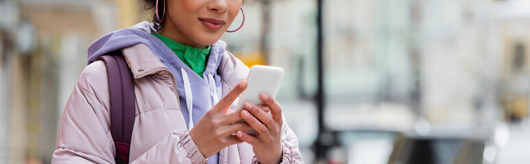 Cropped view of stylish african american woman with smartphone on urban street, banner