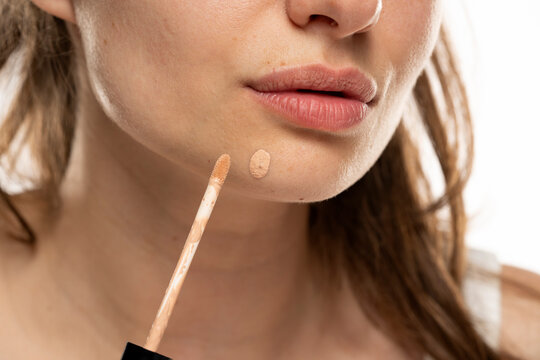 a woman applies concealer to a pimple on her chin