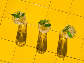 Refreshing summer drinks in crystal glasses with green leaves yellow tile background with harsh...