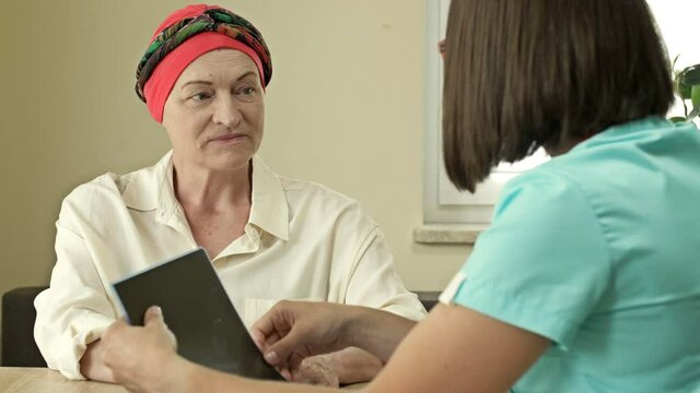 Mature woman with cancer visiting doctor in hospital listening about recovery. Back view of oncologist telling good news to patient after chemotherapy.