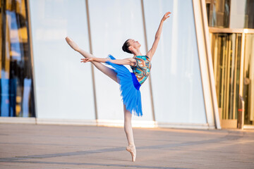 young ballerina in a bright blue tutu is dancing against backdrop of cityscape