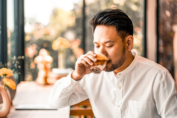 Happy man drinking coffee from cup in cafe.