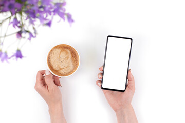 A cup of coffee, two cookies, bells, and a phone in the hand of a woman with a blank white screen. Top view, space for text.