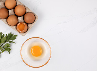 Eggs in a box, a glass cup with a raw egg on a white background. Space for text, top view. The idea of ingredients for a recipe.