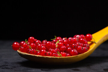 Red currants in a wooden spoon on a black background. Lots of ripe red currants. Delicious berry.
