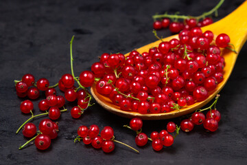 Red currants in a wooden spoon on a black background. Lots of ripe red currants. Delicious berry.