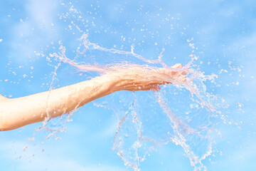 Woman hand with water splash in it against blue sky