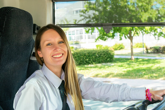 young and beautiful bus driver smiles to camera inside the bus.