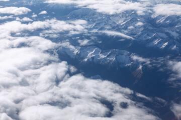 Clouds over the snowy mountains . Mountains view from the airplane window . Alps in the winter season