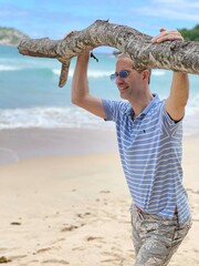 Jeune homme se tenant à une branche de bois sur la plage devant la mer