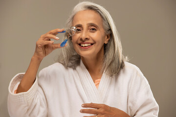 A happy old woman curling her lashes with an eyelash curler.