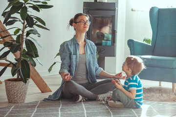 Young mom and child doing yoga together at home sitting on the f