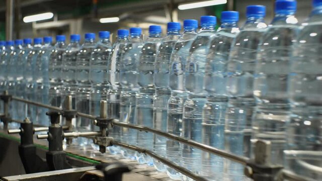 Close-up on the conveyor moving plastic bottles with mineral sparkling water. Production of drinking water at a food processing plant