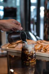 Barista pouring milk into a glass of iced coffee
