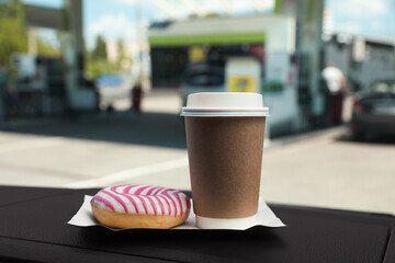 Paper coffee cup and doughnut on car dashboard at gas station