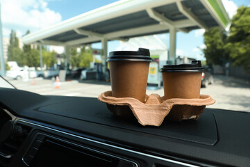 Paper coffee cups on car dashboard at gas station. Space for text