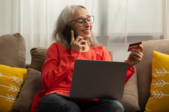 An old woman talking on phone with a card in hand and laptop in  lap.