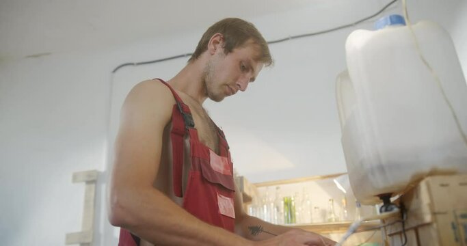 A young handsome guy dressed in overalls makes a glass from recycled bottles cuts glass on a garbage truck environmental project