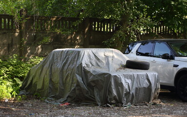 The car is covered with a gray tarpaulin cover