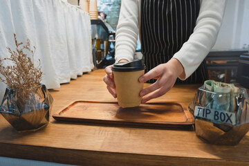 Close up image of a barista serving coffee in a cozy cafe with a tip box nearby