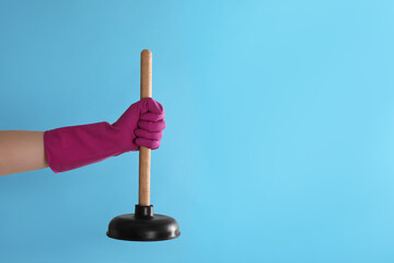 Woman holding plunger on turquoise background, closeup. Space for text