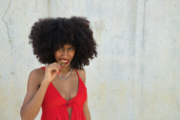 Young, beautiful African-American woman biting a cryptocurrency on a gray cement background.