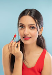 Portrait of beautiful young woman applying lipstick
