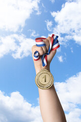 Hand of woman holding gold medal against sky.award and victory concept.copy space