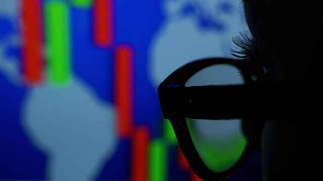 Businesswoman in glasses looks at the stock market charts on the screen.
