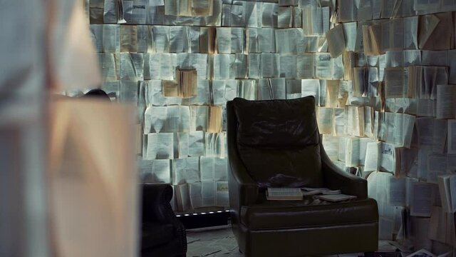 There is an empty black chair in the room. instead of wallpaper, pages from books are pasted on the walls. The apartment is a performance.