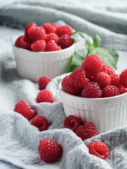 Fresh raspberries in small white cups on a table covered with cloth.