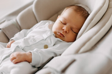 Newborn baby sleeping in a swing, wearing a white pajama.