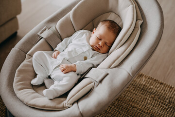 Newborn baby sleeping in a swing, wearing a white onesie pajama.